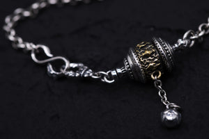 Close-up of a silver & gold Tibetan prayer wheel bracelet on a black background. Intricate details and craftsmanship.