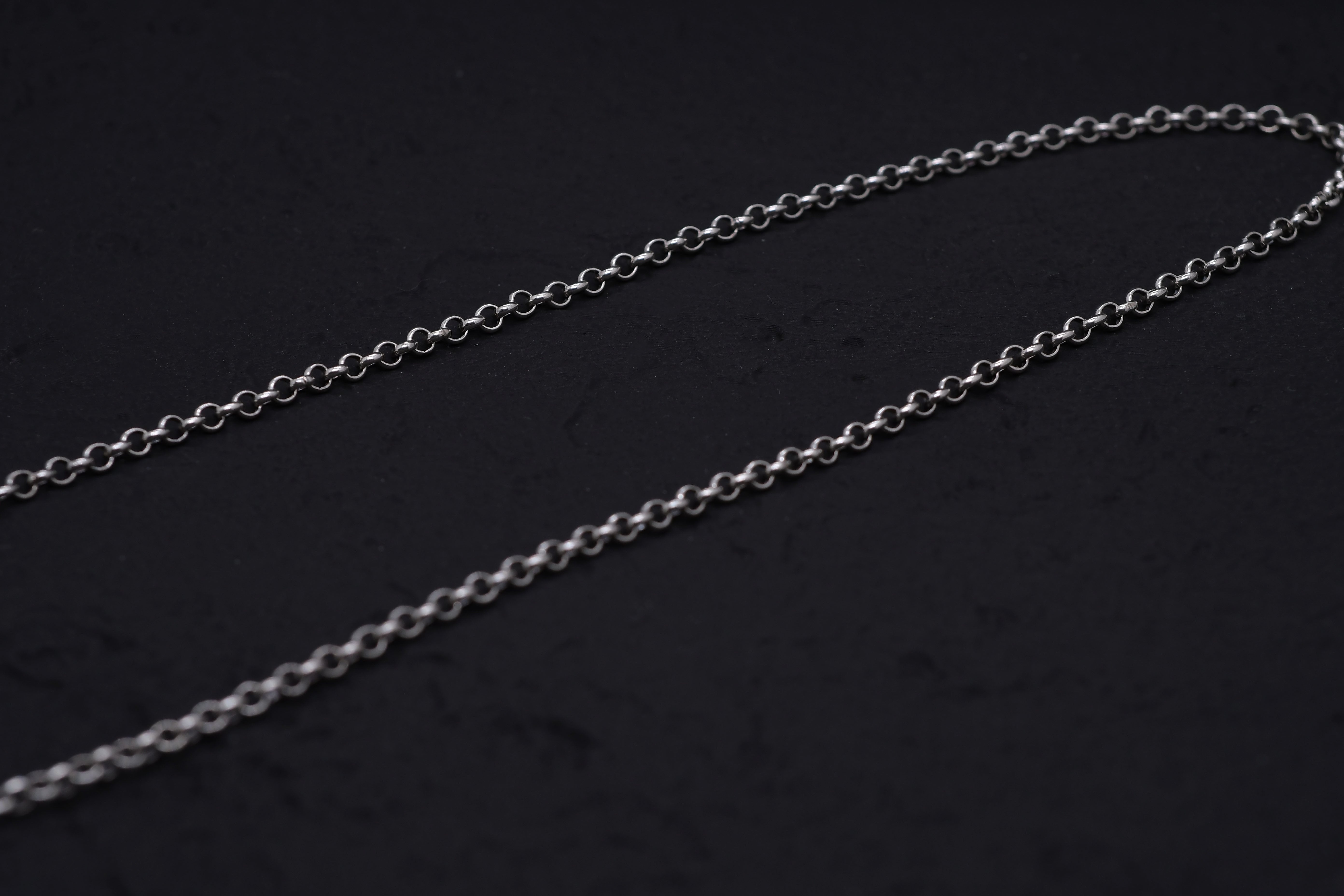 Delicate silver chain gleaming against a dark background. Minimalist, elegant jewelry for layering with Tibetan dzi beads or a protective amulet.