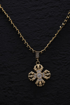 Elegant gold cross pendant necklace with clear gemstones on a black textured background. Tibetan dzi beads inspire this detailed, handcrafted design.