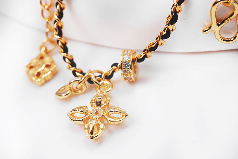 Elegant gold charm bracelet with black cord featuring fleur-de-lis, heart, and other symbolic charms. Buddhist prayer beads for a vintage-inspired look.