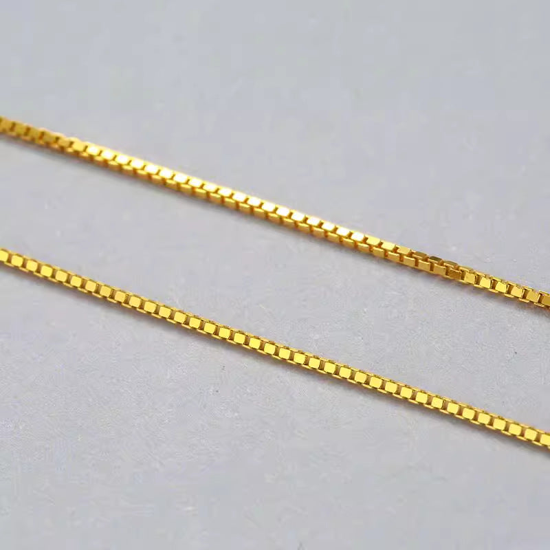 Close-up of a delicate gold box chain with interlocking square links. Simple, elegant design ideal for amulet necklace or prayer beads.
