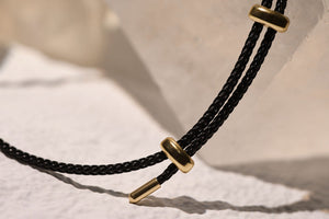 Close-up of a black braided necklace with gold rings and accents, showcasing the intricate design and luxurious details.