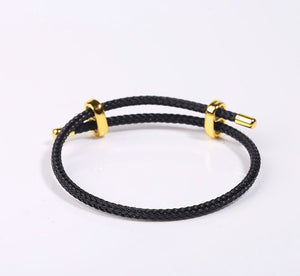 Black braided bracelet with gold accents, drawstring closure, gold beads, and slider on a white background.