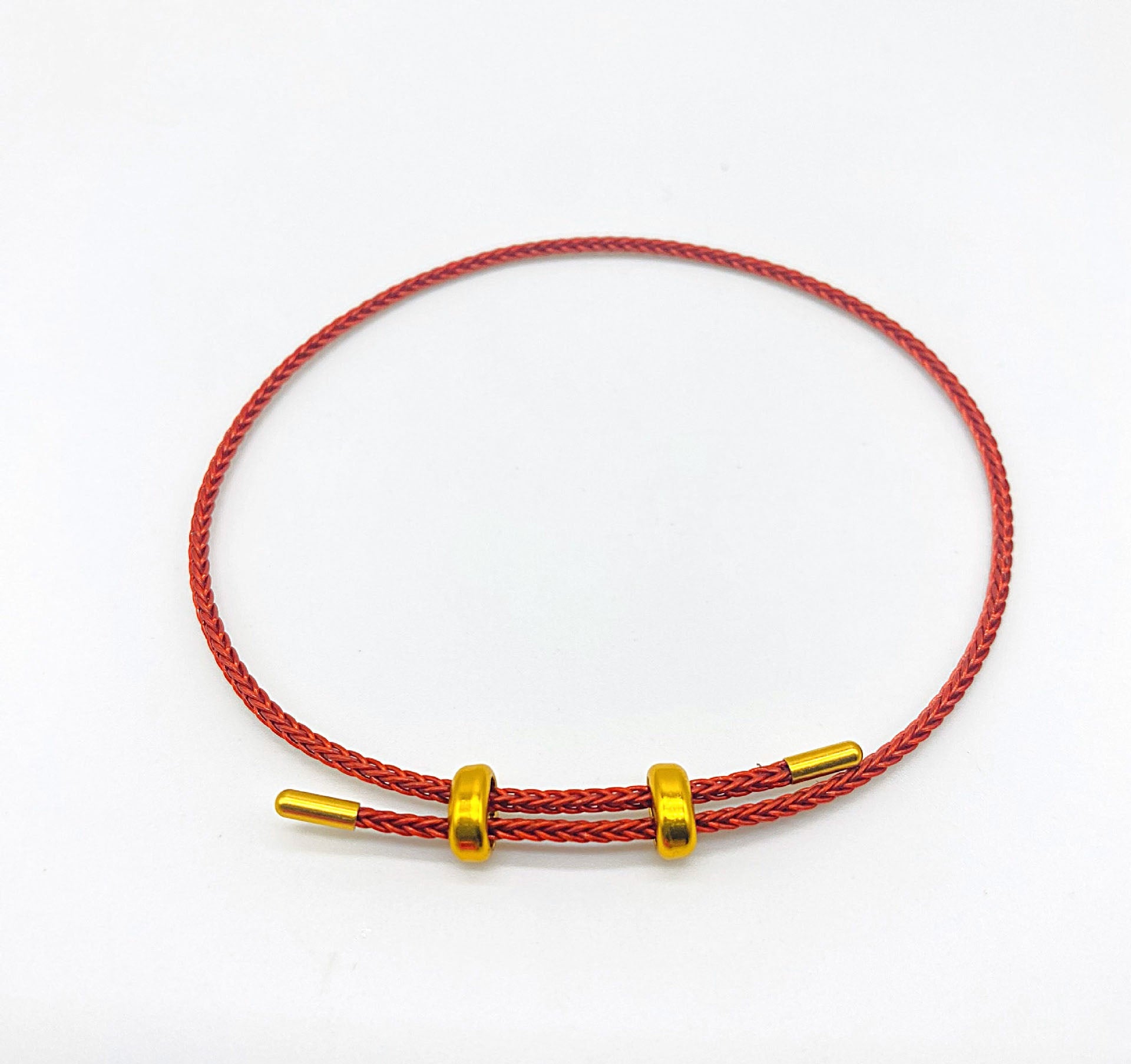 Red braided bracelet with gold beads on white background.