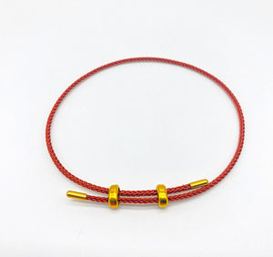 Red braided bracelet with gold beads on white background.