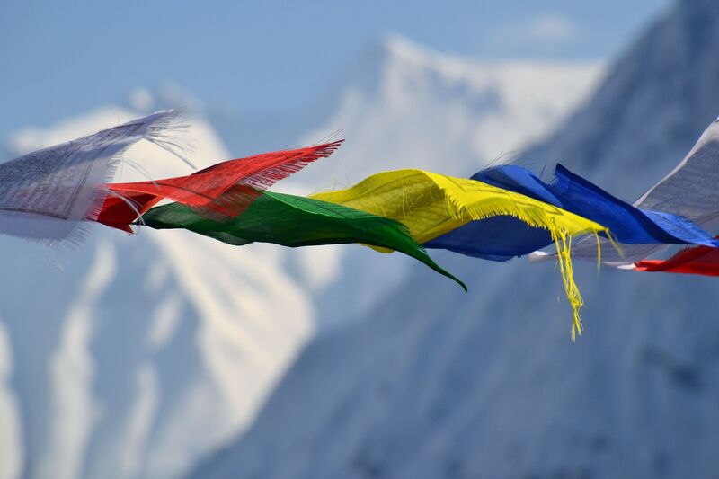 Colorful Tibetan prayer flags flutter in the Himalayan wind against a backdrop of snow-capped mountains, carrying sacred blessings and manifesting intentions.